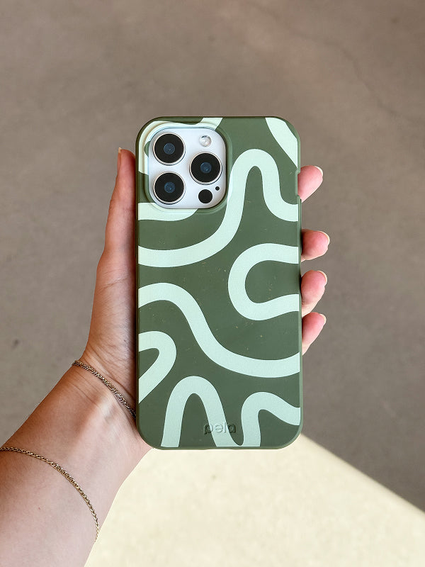 Close-up of a hand holding an iPhone with the Wiggles Phone Case from Pela's Forest Floor Collection, featuring pale green abstract squiggles on a mossy green background.