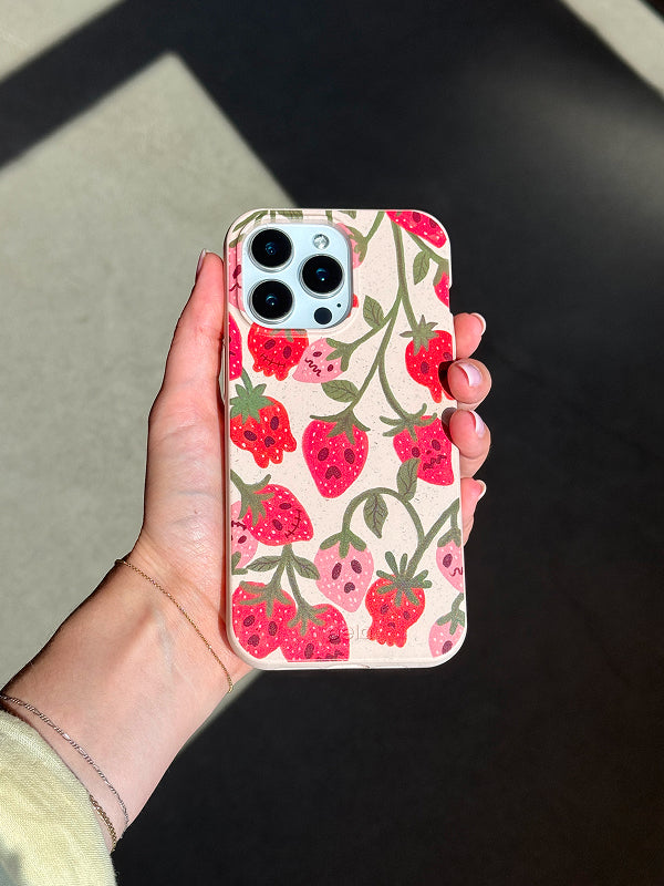 Hand holding a phone with the Strawboories Phone Case by Pela, featuring a playful design of bright red strawberries with spooky ghost faces on a cream background.