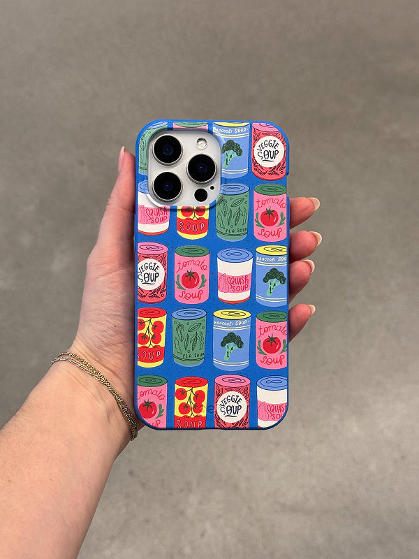 Hand holding a phone featuring the Soup Stories Phone Case, decorated with colorful illustrated soup cans on a bright blue background.