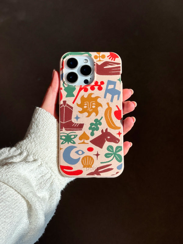 Hand holding the Pela x Whitney Nettles Junk Drawer Phone Case featuring a colorful folk-art inspired design with suns, horses, boots, and playful shapes on a neutral background.